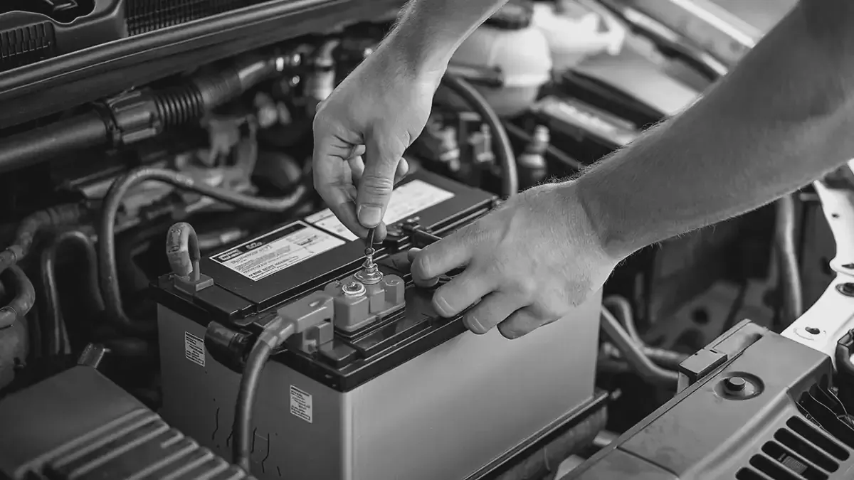 Handen maken de klem van een accupool vast in de motorruimte